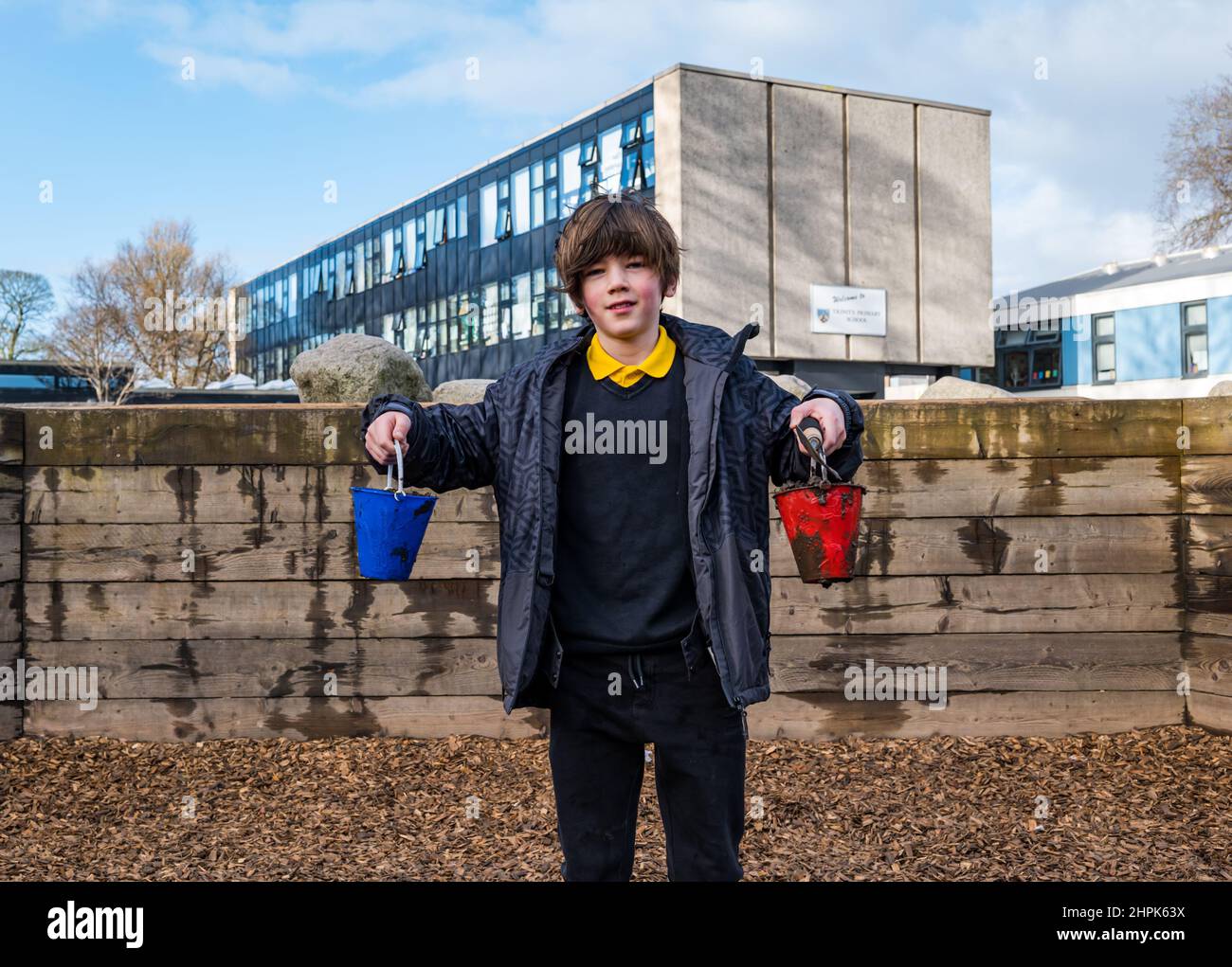 Trinity Primary School, Edimburgo, Scozia, Regno Unito, 22 febbraio 2022. Topsoil Botanico per le scuole: Lo scavo durante il Royal Botanic Garden Biomes Project dà luogo a un'eccedenza di topsoil di 50 tonnellate che viene data a scuole, allotments & organizzazioni della comunità da Balfour Beatty. Una consegna di 5 tonnellate avviene presso la Trinity Primary School per trasportare il suolo o la terra per riempire piantatrici nel giardino della scuola per gli allievi per coltivare le verdure. Gli allievi primari 4 usano contenitori di tutte le forme e dimensioni per spostare la terra per riempire le piantatrici; lavoro di squadra è richiesto Foto Stock