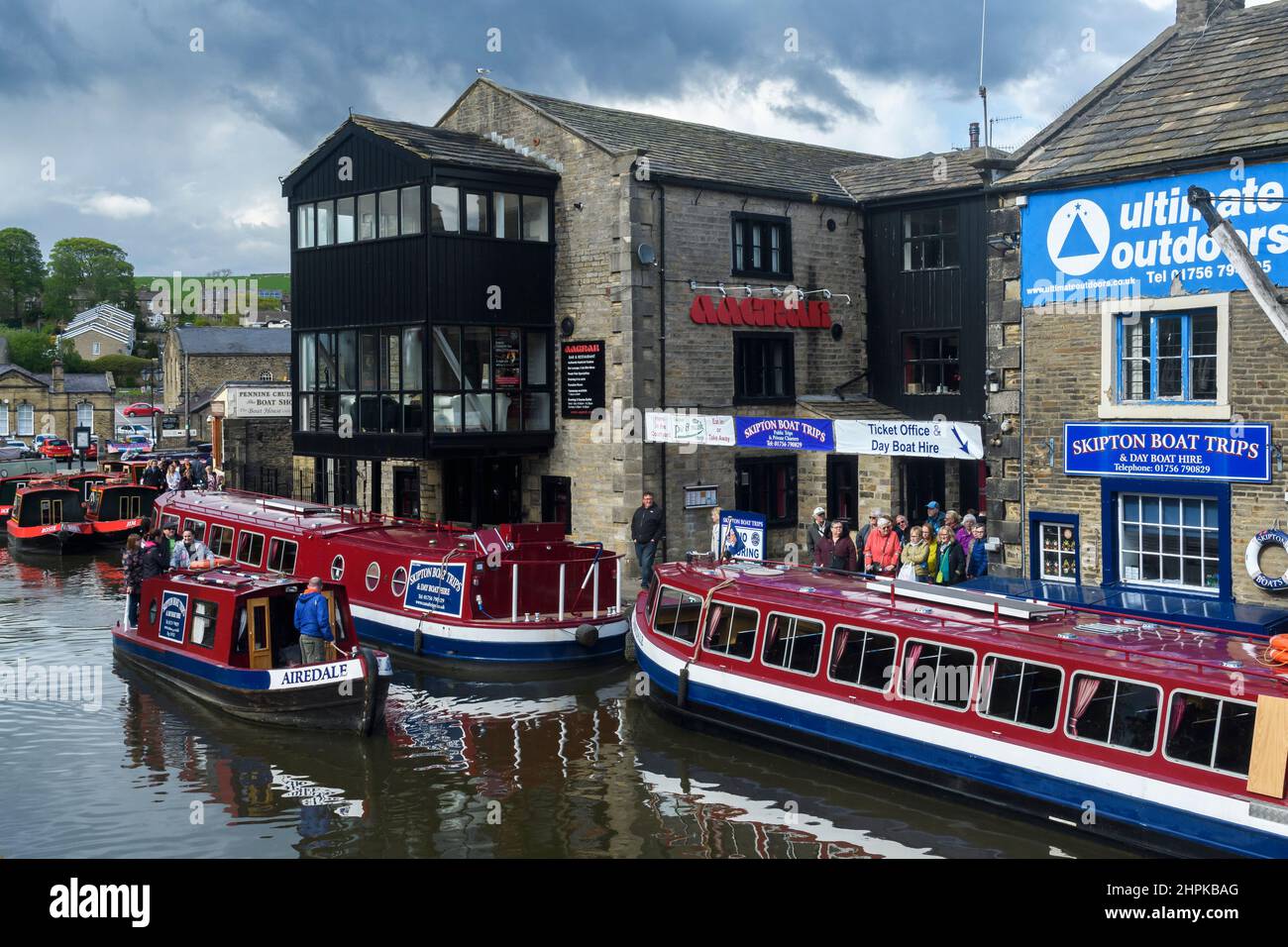 Gita turistica in acqua (auto-drive barca a noleggio rossa, uomini donne che fanno la fila, barche ormeggiate, ormeggi) - panoramico Leeds-Liverpool Canal, Yorkshire, Inghilterra UK Foto Stock