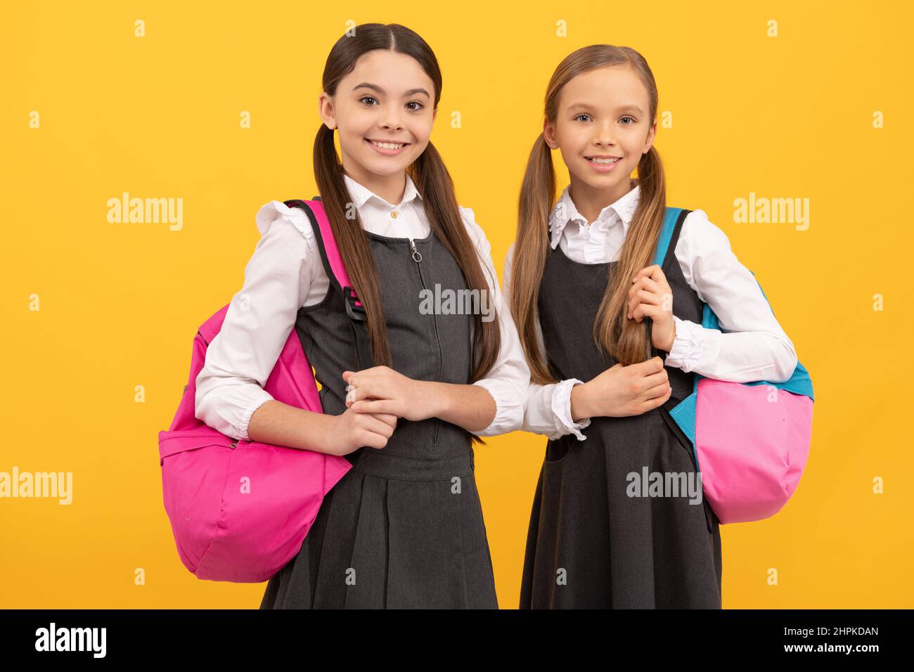 I capretti felici trasportano i sacchetti della scuola in uniforme di modo formale sfondo giallo, di nuovo alla scuola Foto Stock