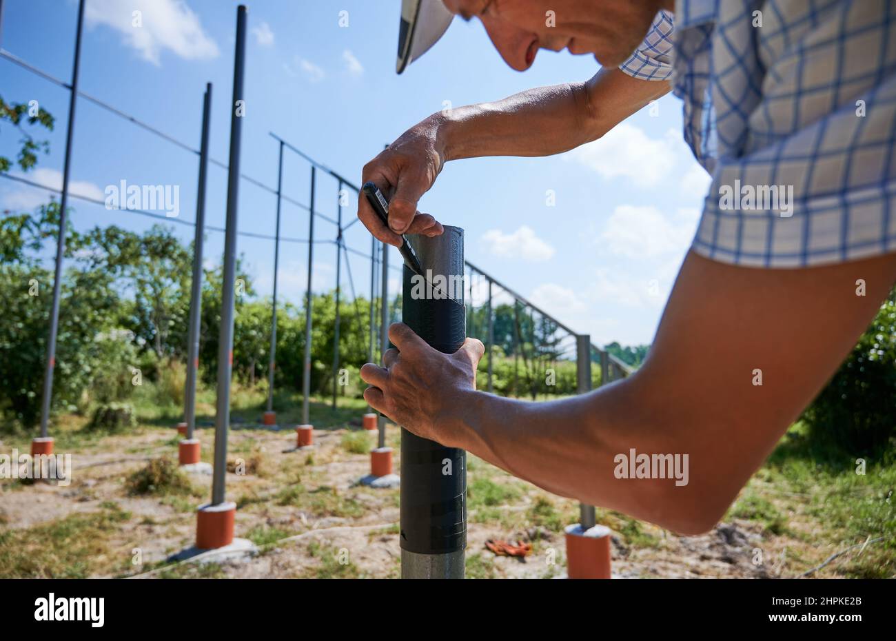 Primo piano dell'installatore solare MAN che traccia la linea sul tubo meatale con pennarello. Maschio lavoratore marcatura struttura di supporto per i moduli solari durante l'installazione del sistema di pannelli solari in campo erboso. Foto Stock