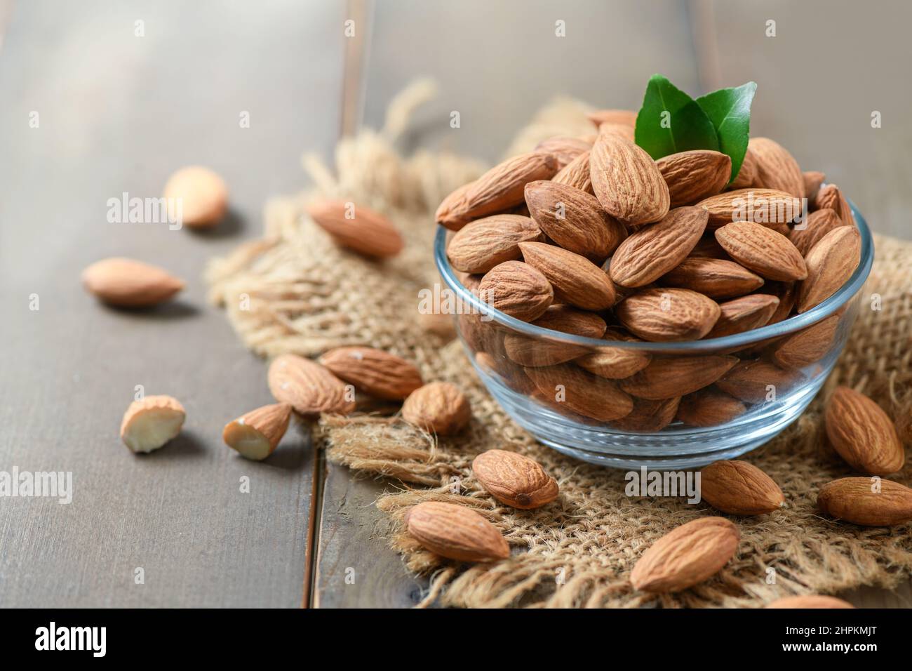 Noce di mandorle con foglie in bicchiere di vetro su sfondo di legno. Sono altamente nutritivi e ricchi di grassi sani o di colestie ad alta densità di lipoproteine (HDL) Foto Stock