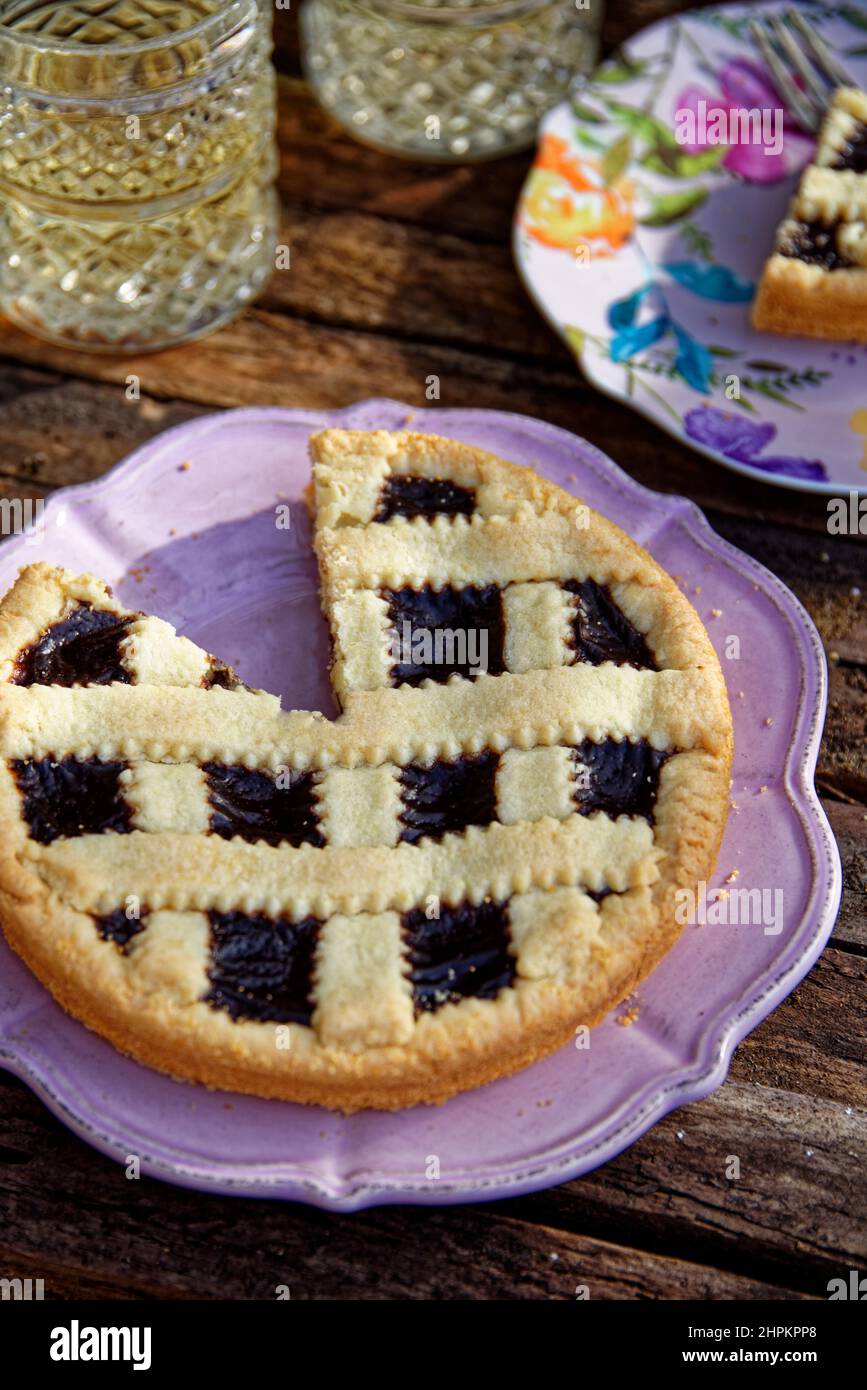 Torta di pasticceria alla crema di cioccolato servita in un piatto rosa su tavola di legno, fette di torta in campo su un piatto fiorito, due bicchieri di tè freddo Foto Stock