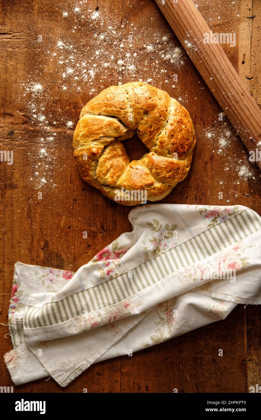 Pane fatto in casa a forma di anello in legno posato con spina di laminazione, un po' di farina, tessuto floreale Foto Stock