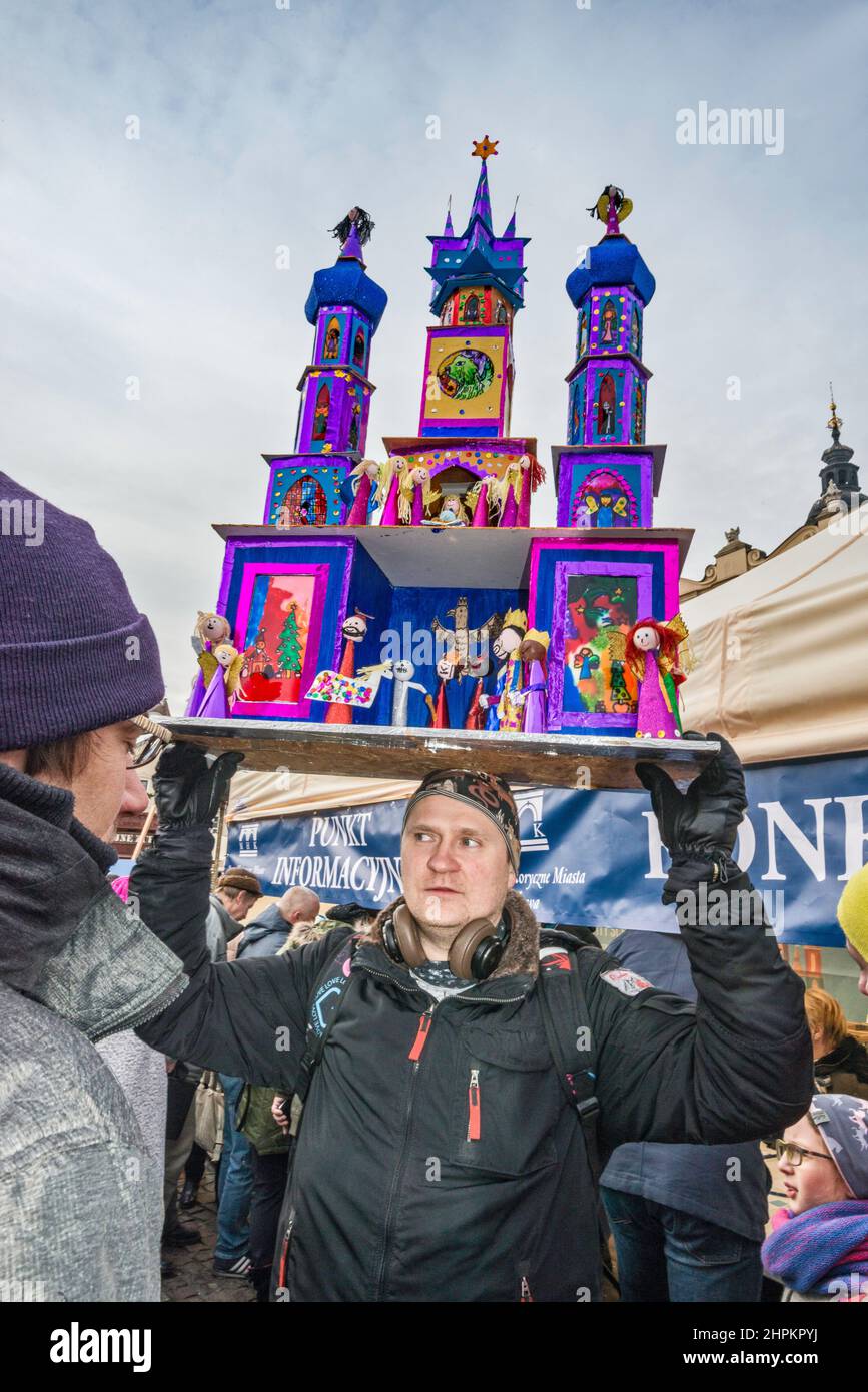 Uomo che porta la scena natività di Szopka in testa per la mostra durante il concorso annuale di dicembre, evento incluso nella lista del Patrimonio Culturale dell'UNESCO, al monumento Adam Mickiewicz, Piazza del mercato principale, Kraków, Polonia Foto Stock