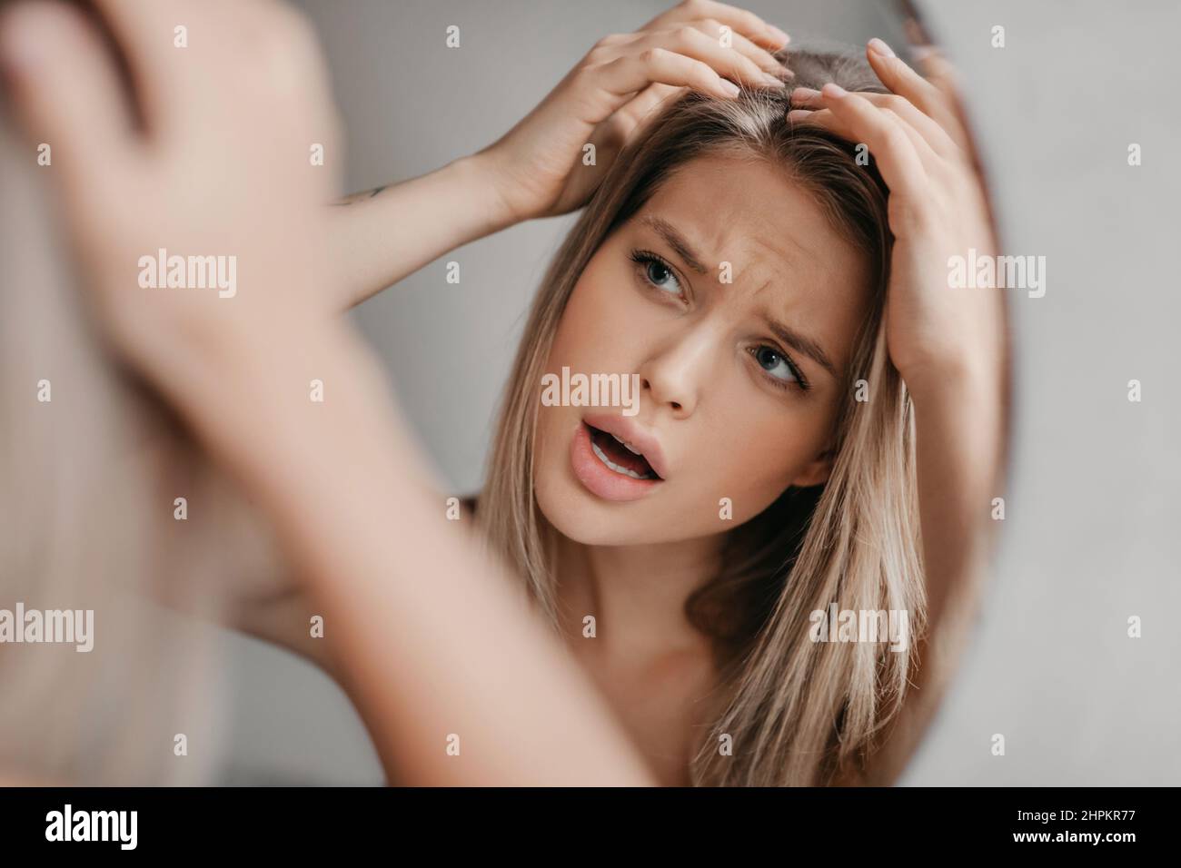 Donna frustrato cercando capelli fiocchi che soffrono di problema di forfora, guardando la sua riflessione nello specchio in bagno Foto Stock