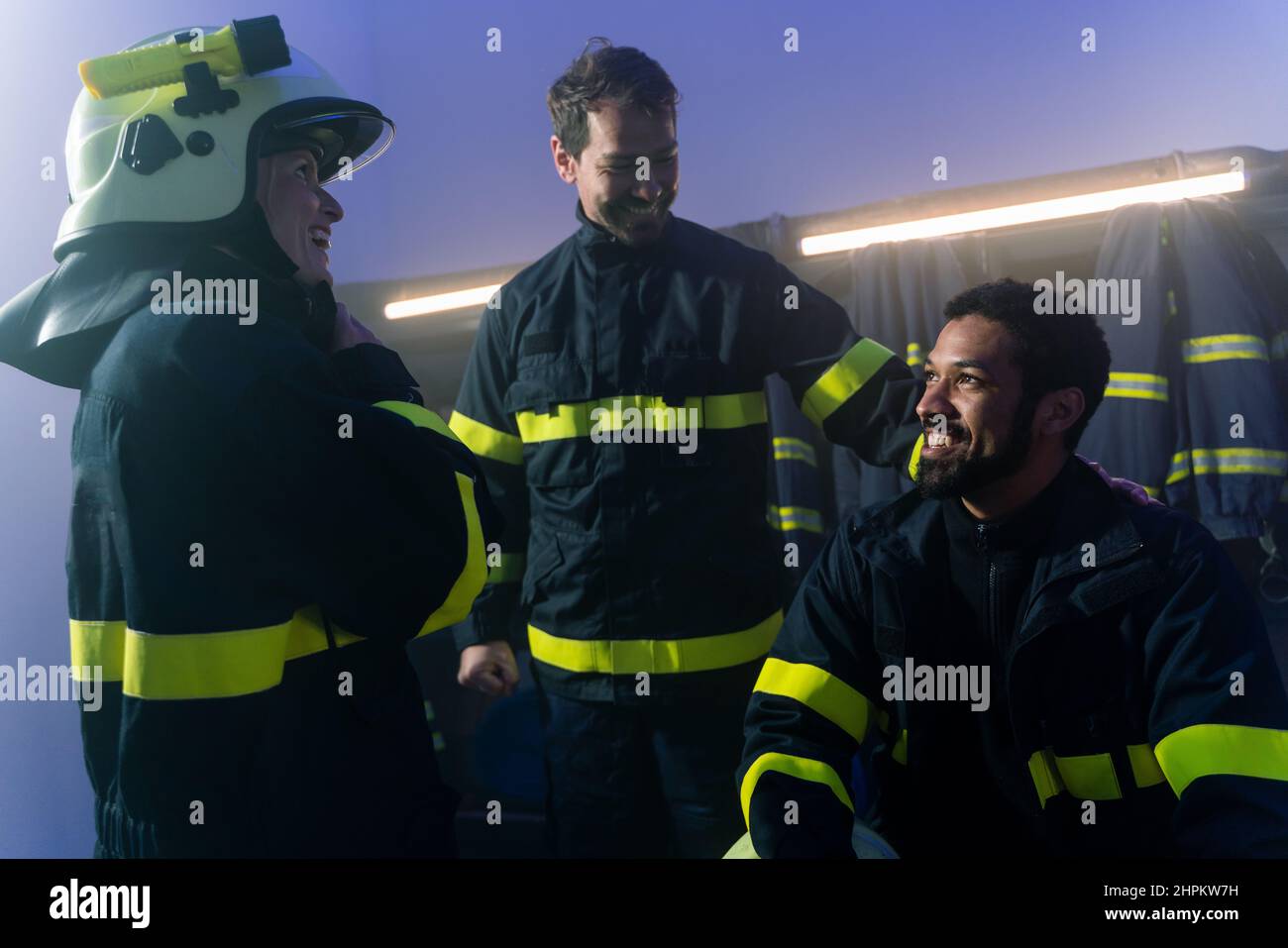 Felici vigili del fuoco uomini e donne che parlano dopo l'azione al chiuso nella stazione dei vigili del fuoco Foto Stock