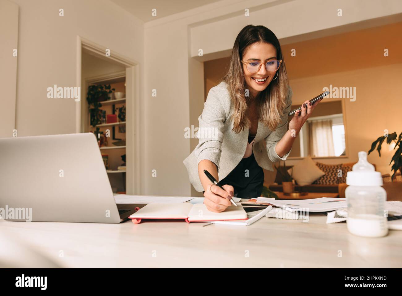 Felice interior designer che parla al telefono nel suo ufficio domestico. Donna d'affari creativa che prende appunti durante una telefonata con i suoi clienti. D femmina Foto Stock