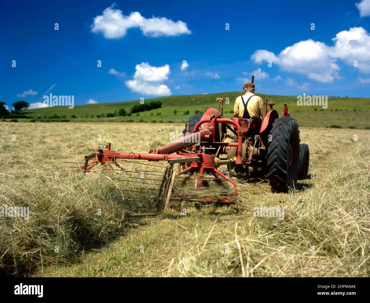 L'attività di fine estate di cazzo del fieno per l'imballaggio utilizzando un vecchio trattore rosso a Glaister Farm vicino Darvel in East Ayrshire, Scozia. Foto Stock