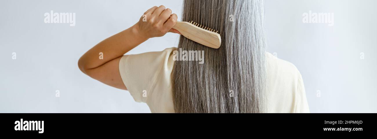Lady pennelli capelli lisci argento in piedi su sfondo grigio chiaro Foto Stock