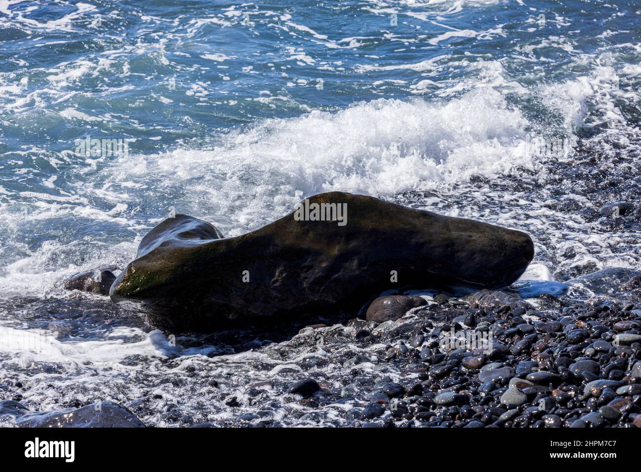 Marea che si infrangono su una roccia di forma insolita su una spiaggia di pietra vicino Playa de San Juan, Tenerife, Isole Canarie, Spagna Foto Stock