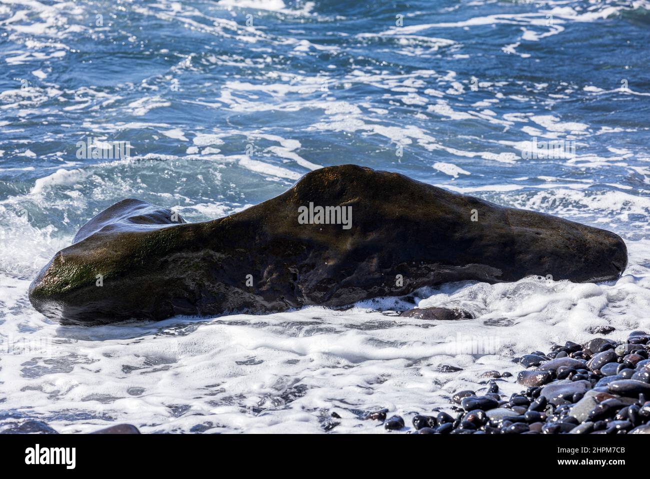Marea che si infrangono su una roccia di forma insolita su una spiaggia di pietra vicino Playa de San Juan, Tenerife, Isole Canarie, Spagna Foto Stock
