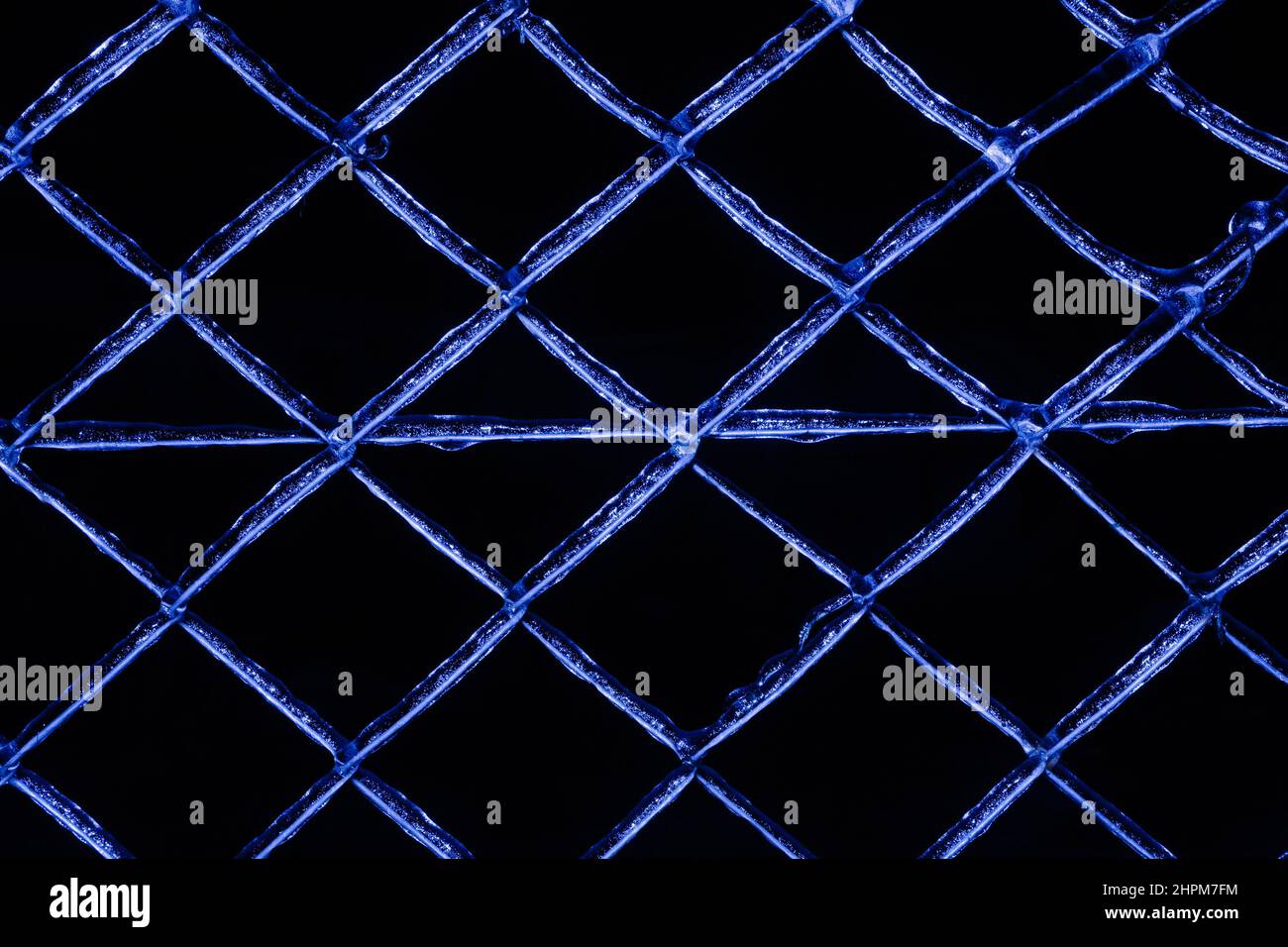Foto di una recinzione di metallo congelato di colore blu ricoperta di ghiaccio su sfondo nero. Foto Stock