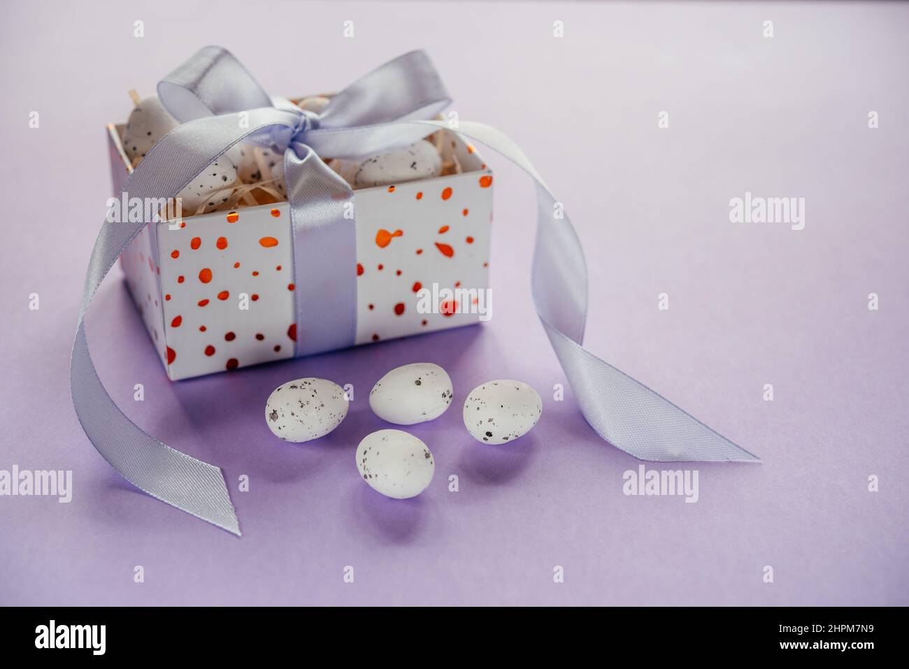 Pasqua creativa layout con uova di Pasqua in una confezione regalo con nastri di lavanda blush su sfondo viola chiaro Foto Stock