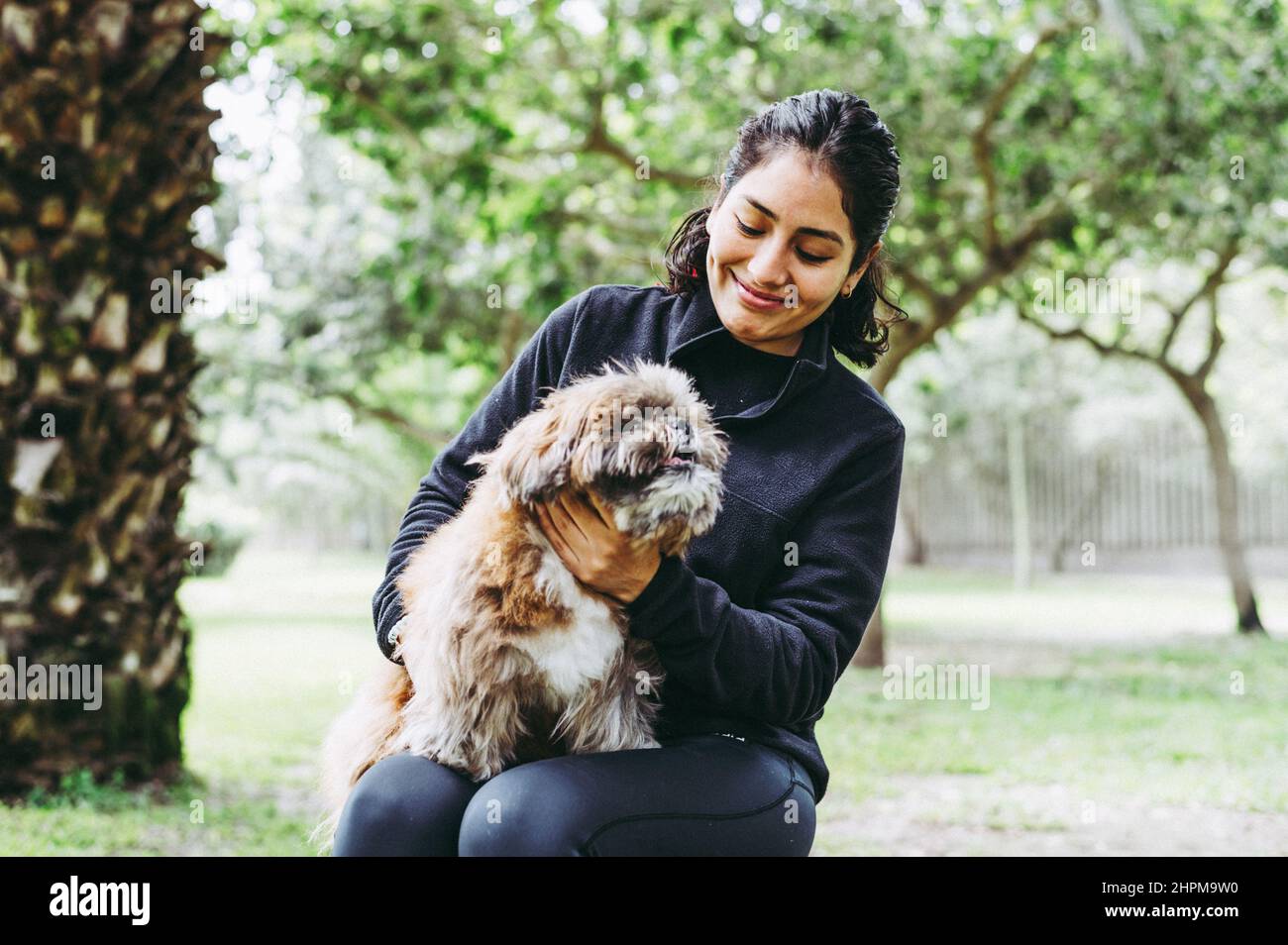 La giovane donna carina sta abbracciando il suo piccolo cucciolo. Amore tra proprietario e cane. Foto all'aperto nel parco, fuoco selettivo. Concetto di stile di vita Foto Stock