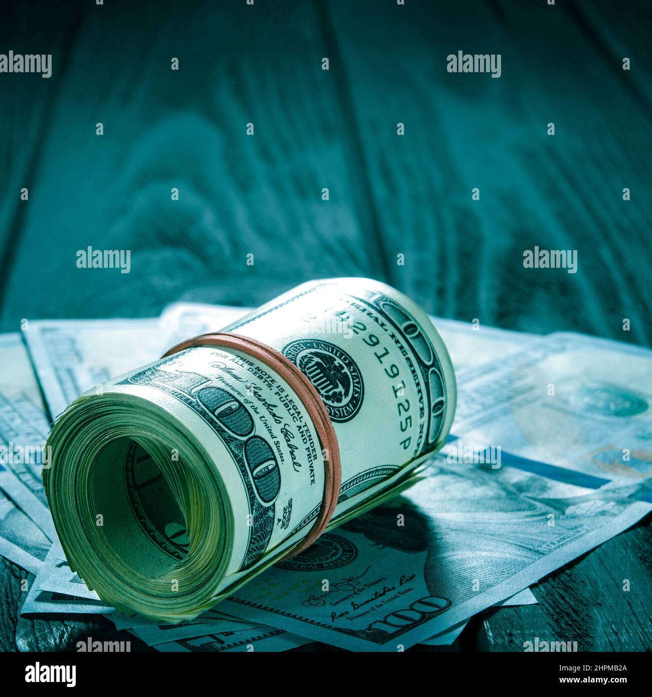 Un rotolo delle fatture e delle monete del dollaro sopra le altre fatture su una scrivania. Evidenziare per la bolletta del centinaio di dollari. Un rotolo spesso di vecchie banconote da cento dollari legato Foto Stock