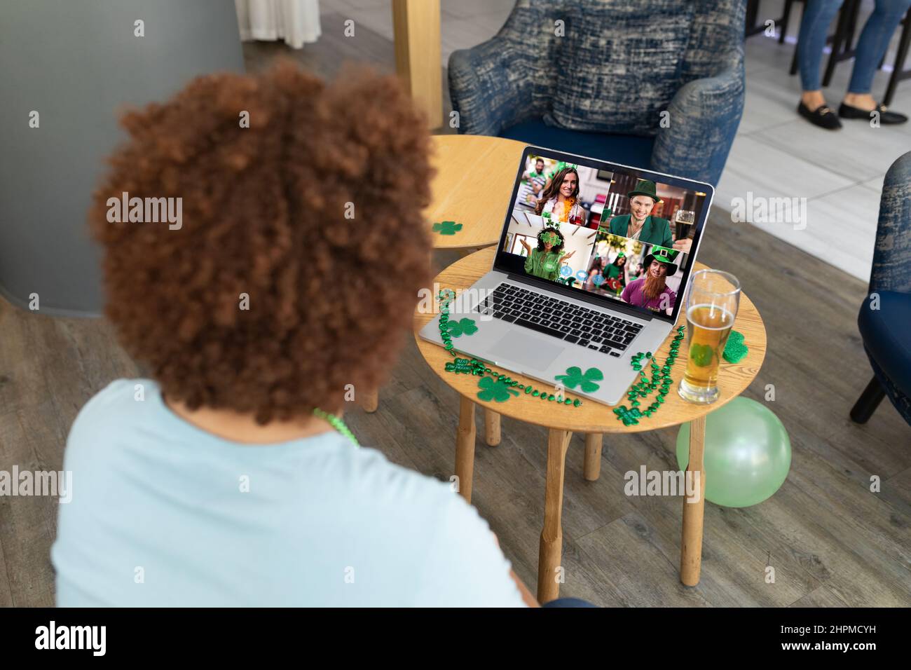 Un uomo misto che festeggia la giornata di san patrizio facendo videochiamate con gli amici su un computer portatile al bar Foto Stock