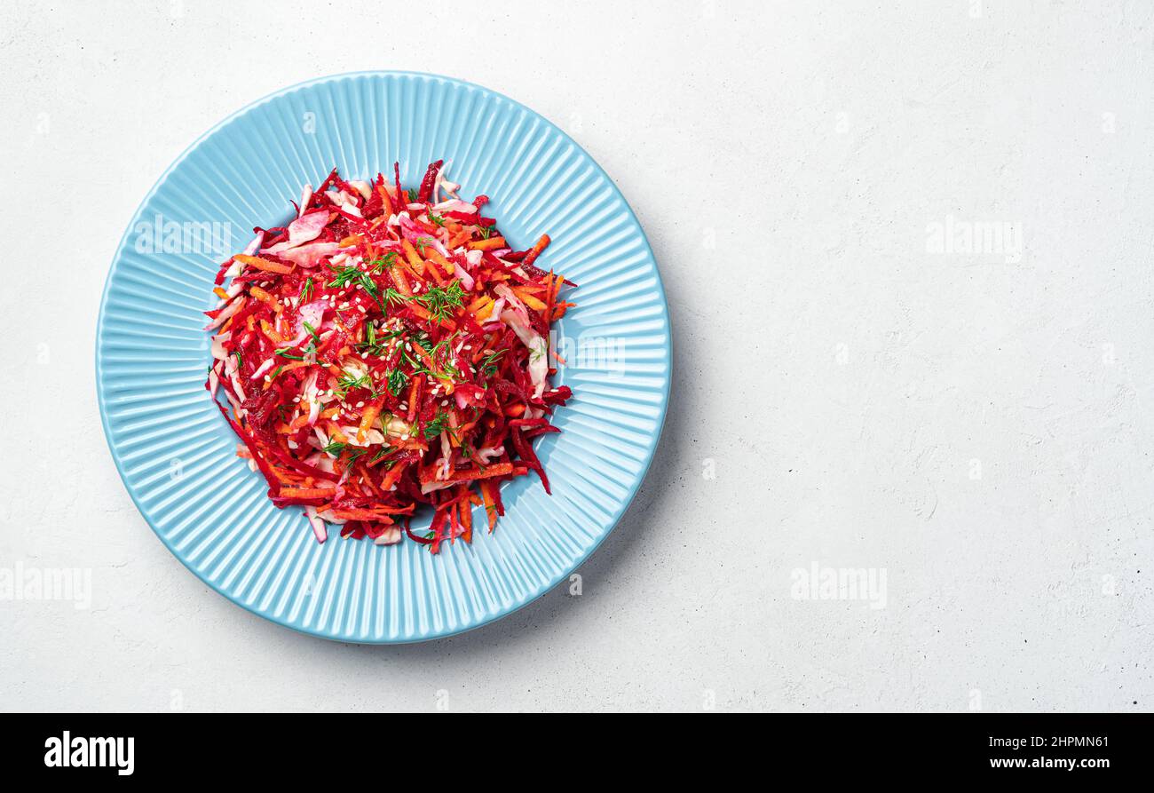 Insalata di verdure fresche con cavolo, barbabietole, carote e semi di sesamo in un piatto blu su sfondo grigio. Pulizia, insalata dietetica. Vista dall'alto, copia Foto Stock