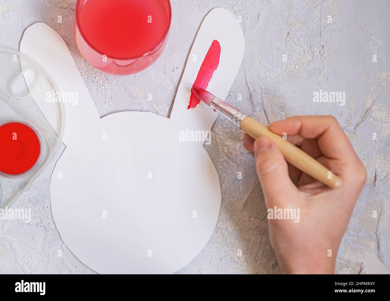 la mano femminile dipinge un coniglietto pasquale di carta con vernice rossa. Foto Stock