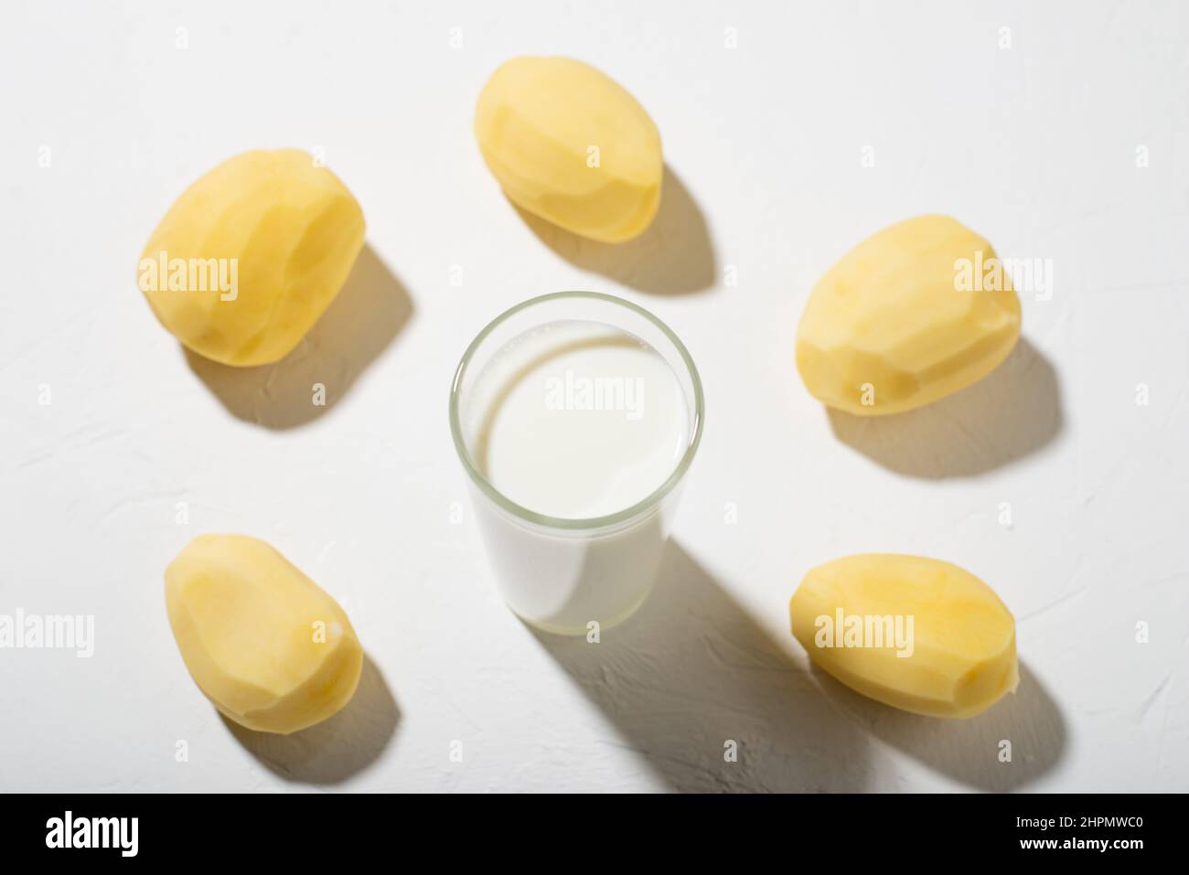 Alternativa al latte di patate. Un bicchiere di latte e una patata cruda su sfondo bianco. Foto Stock