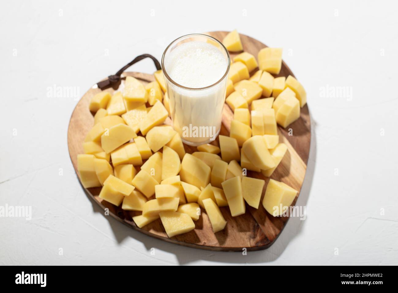 Concetto di latte di patate. Latte alternativo. Un bicchiere di latte su un asse di legno con patate crude tritate. Foto Stock