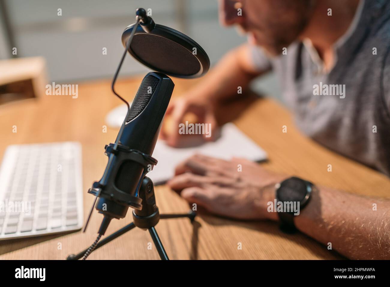 Microfono con filtro pop primo piano foto con un uomo che legge il testo e registra la voce utilizzando un computer desktop. Reco audio moderno da studio Foto Stock