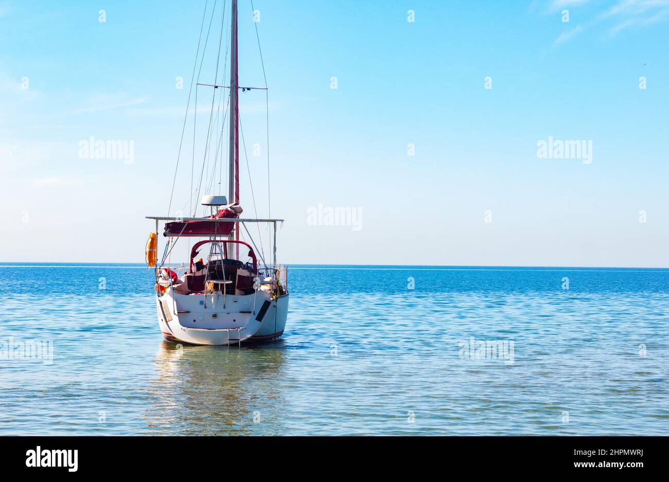 Foto di barca a vela di colore bianco con vele abbassate che sgocciolano in mare aperto a metà giornata. Foto Stock