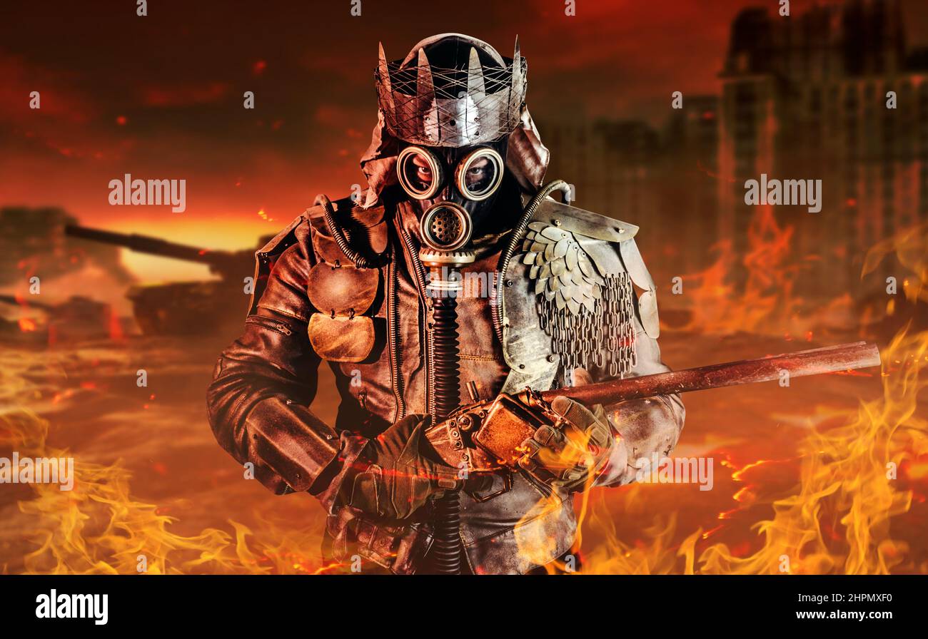 Foto di guerriero post apocalittico con giacca blindata e corona di rottami in piedi con fucile su sfondo distrutto città burning. Foto Stock