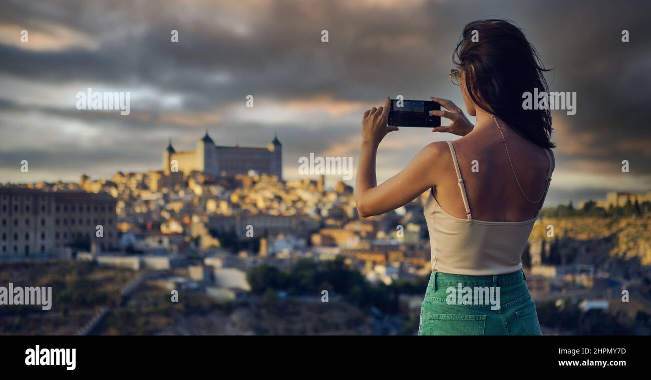 Retro vista posteriore giovane donna tenere cellulare scattare foto godere Toledo vista paesaggio urbano, dalla fotocamera smartphone. Momento di cattura turistico, fotografando famoso Foto Stock