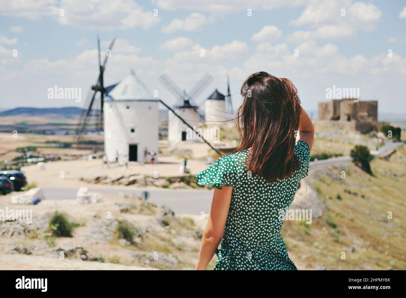 Posteriore vista posteriore giovane donna che si posa contro famoso vecchio sfondo mulini a vento nella città di Consuegra. Castilla-la Mancha. Toledo, Spagna. Attrazioni turistiche AN Foto Stock