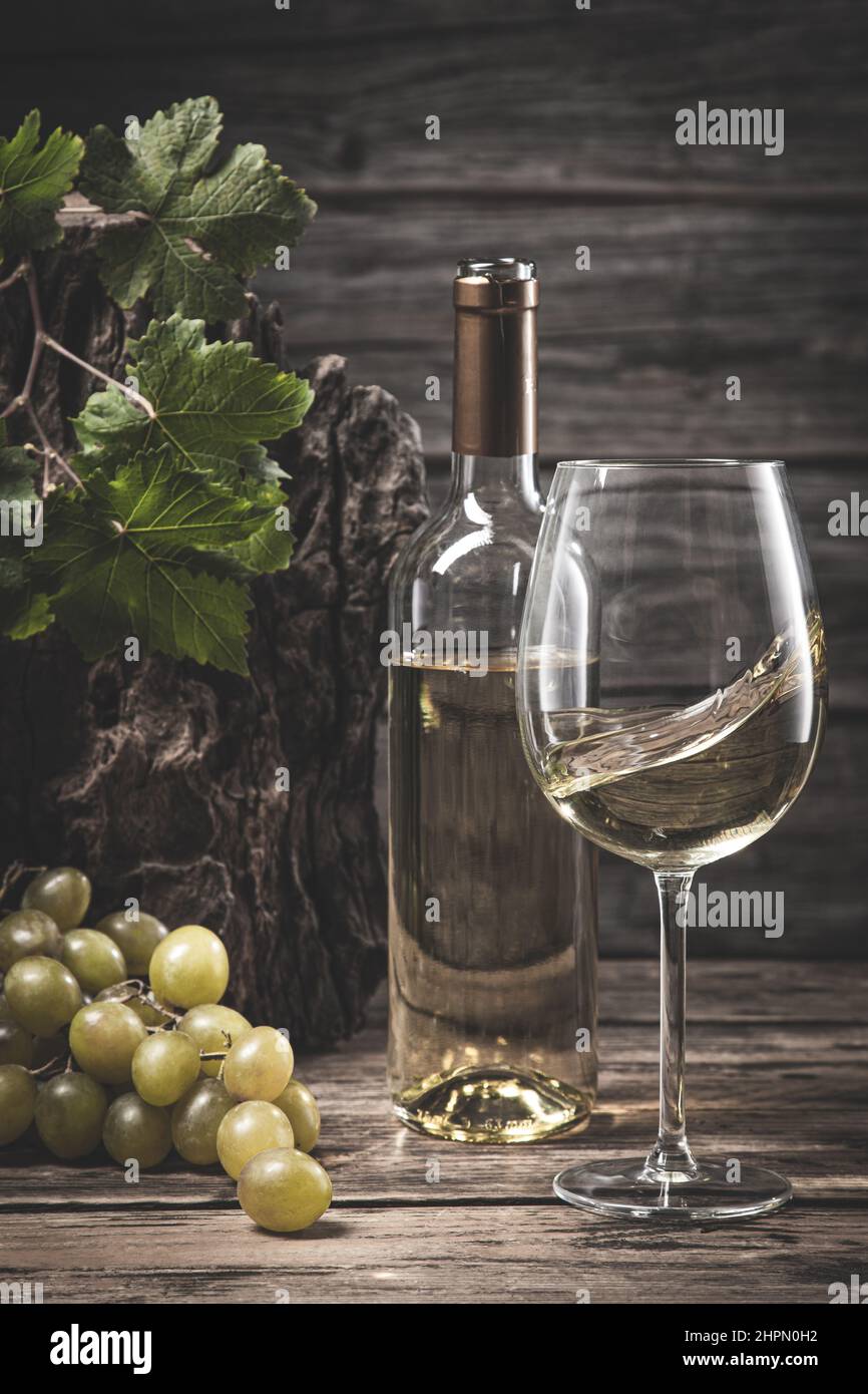 Bicchiere di vino e bottiglia di vino bianco con uva e vite su sfondo di legno. Formato verticale. Foto Stock