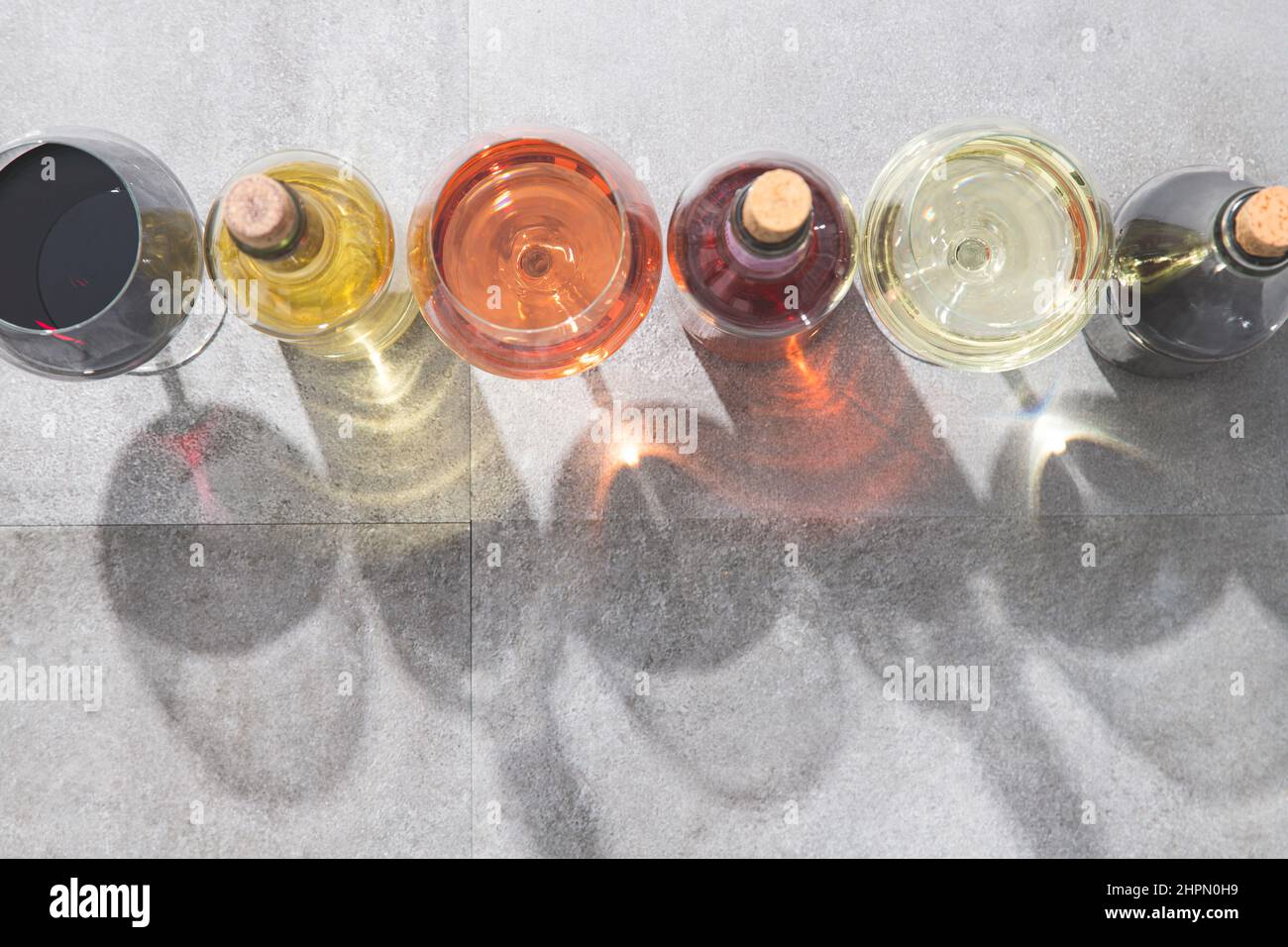 Vino rosso, bianco e rosato in bicchieri e bottiglie con ombre profonde su fondo di cemento e spazio per la copia. Concetto di vini. Foto Stock