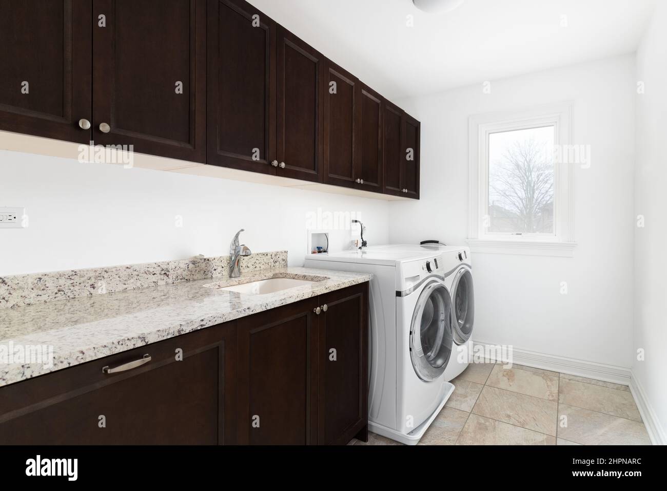 Una lavanderia con lavatrice e asciugatrice bianca, armadi in legno di mogano scuro e ripiani in granito. Foto Stock