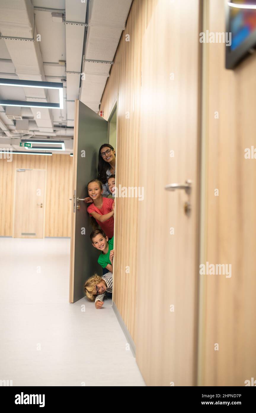 Insegnante con bambini che guardano fuori dalla classe nel corridoio Foto Stock
