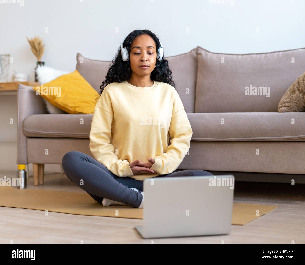 Donna afroamericana che ascolta musica in cuffia mentre medita con il portatile a casa Foto Stock