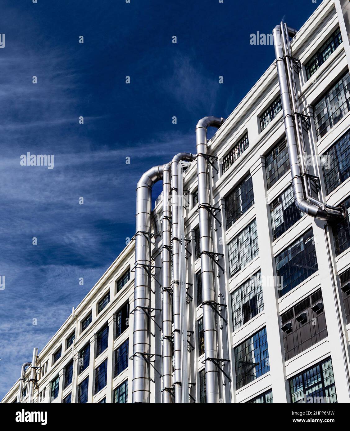 Vista ad angolo basso dell'esterno di un edificio industriale a più piani con un suggestivo cielo blu. Finestre e tubi di sfiato in argento. Foto Stock