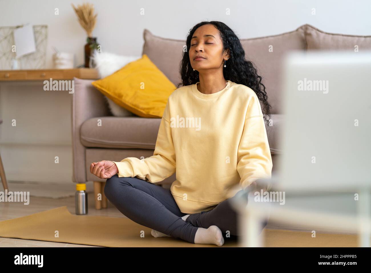 Giovane donna afro-americana seduta in loto posa sul tappeto in soggiorno mentre meditating Foto Stock