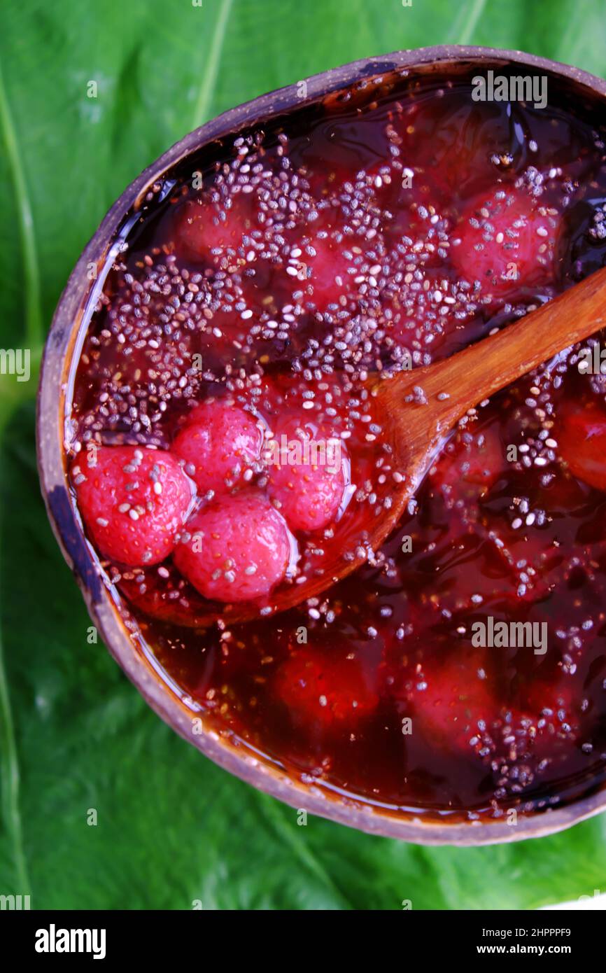 Vista dall'alto fragole rosse zuccherate in ciotola che fanno da conchiglie di cocco su foglia verde, frutta rossa fresca da Lat per giorno d'estate, cibo yummy Foto Stock