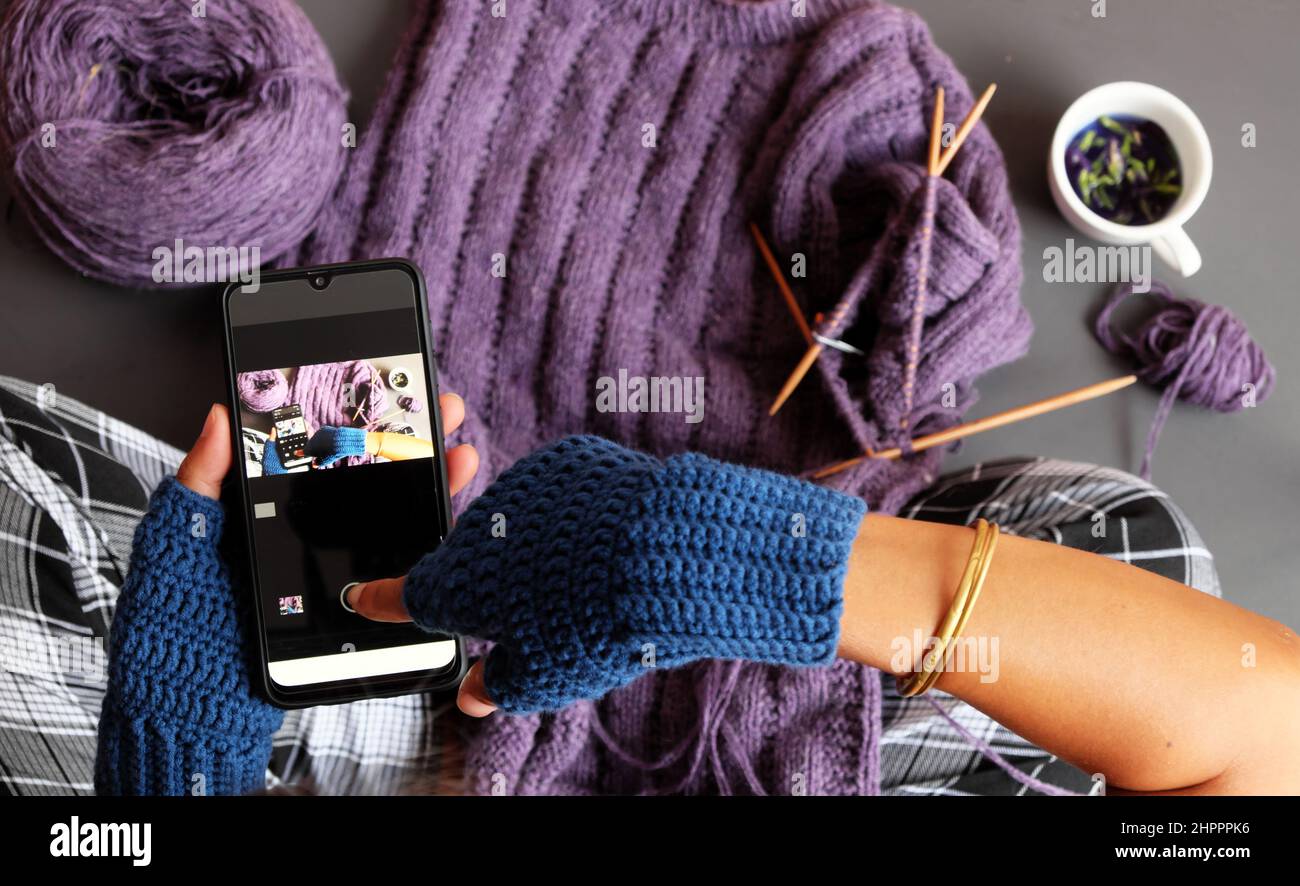 Vista dall'alto donna indossate il crochet mitten blu, il pullover viola lavorato a maglia in regalo in inverno, lo smartphone con stampa a mano chiusa per scattare foto in tonalità scure Foto Stock