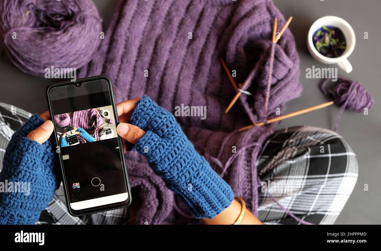 Vista dall'alto donna indossate il crochet mitten blu, il pullover viola lavorato a maglia in regalo in inverno, lo smartphone con stampa a mano chiusa per scattare foto in tonalità scure Foto Stock