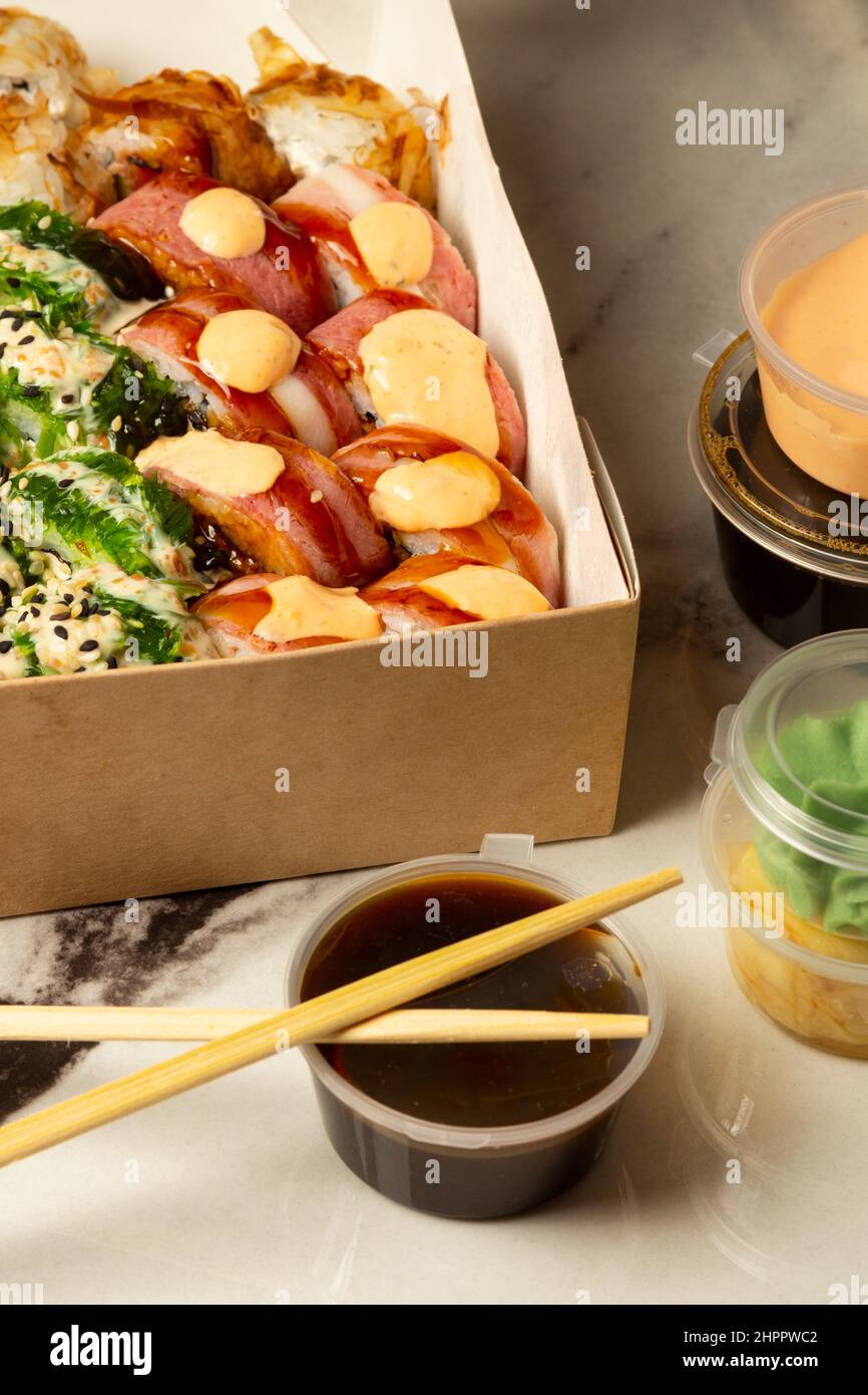 Scatola con rotoli di sushi accanto a contenitori con salse su un tavolo di marmo chiaro Foto Stock