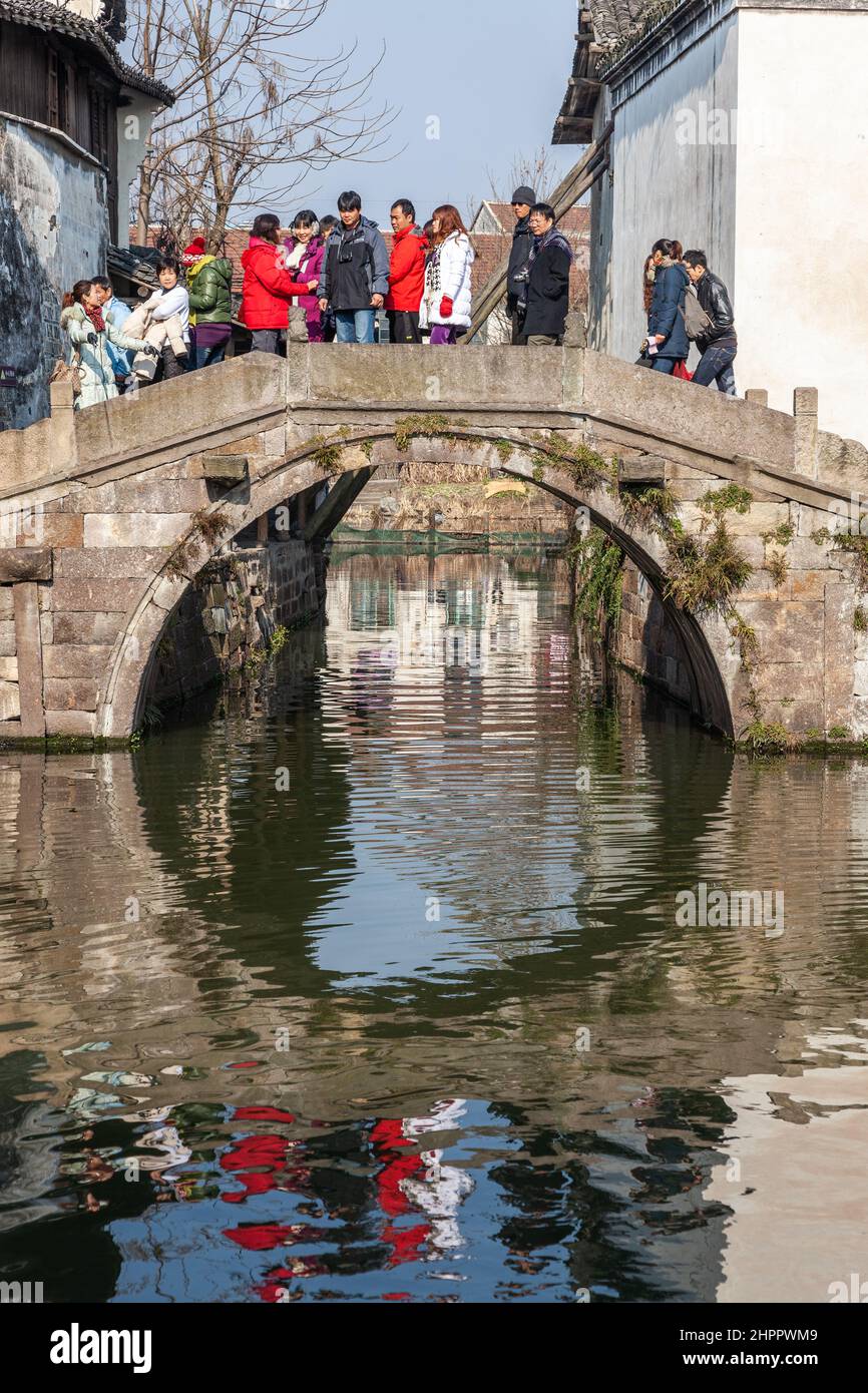 Gruppo di turisti che attraversano un ponte di pietra che attraversa un canale nel villaggio acquatico di Wenzhou, Cina Foto Stock