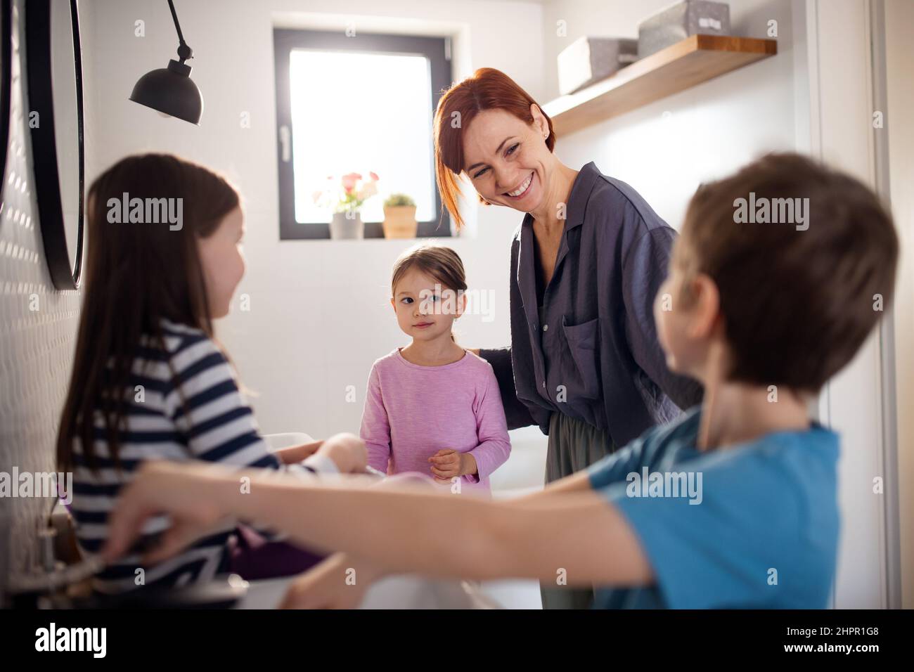 Madre con tre bambini piccoli in bagno, mattina concetto di routine. Foto Stock