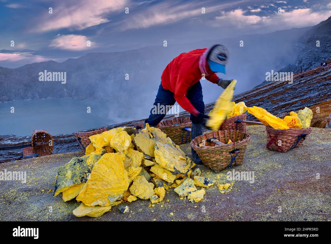 Minatori di zolfo che salgono e scendono fino al cratere. Un uomo mette circa 10 kg di pietra giallastra nel suo cesto, prima di scendere il pendio di montagna t Foto Stock