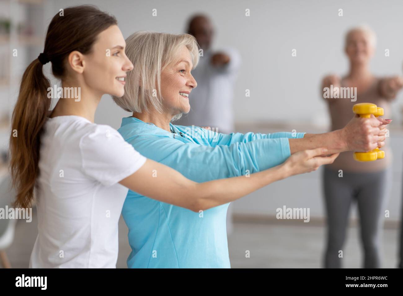 Vista laterale dell'allenatore di fitness che aiuta la donna anziana mentre si esercita Foto Stock