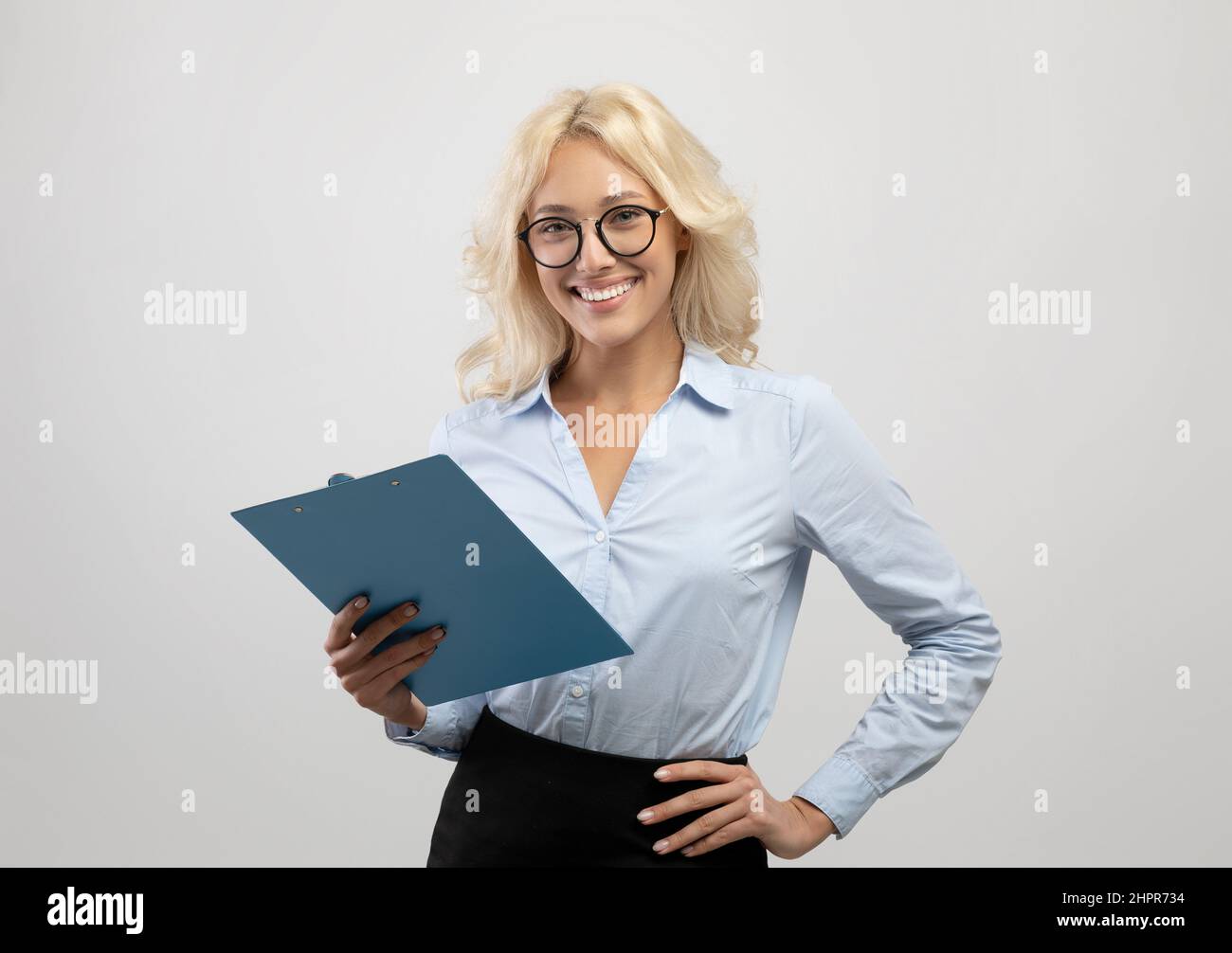 Ritratto di giovane donna d'affari di successo che posa con appunti in mano e sorridendo alla macchina fotografica Foto Stock