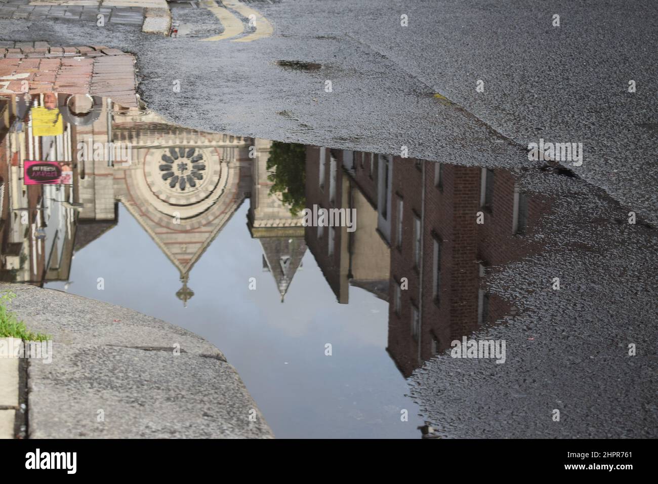 Chiesa e case riflessione in acqua. Foto urbana capovolta. Effetto specchio in una pozzanghera. Dublino. Irlanda. Foto Stock