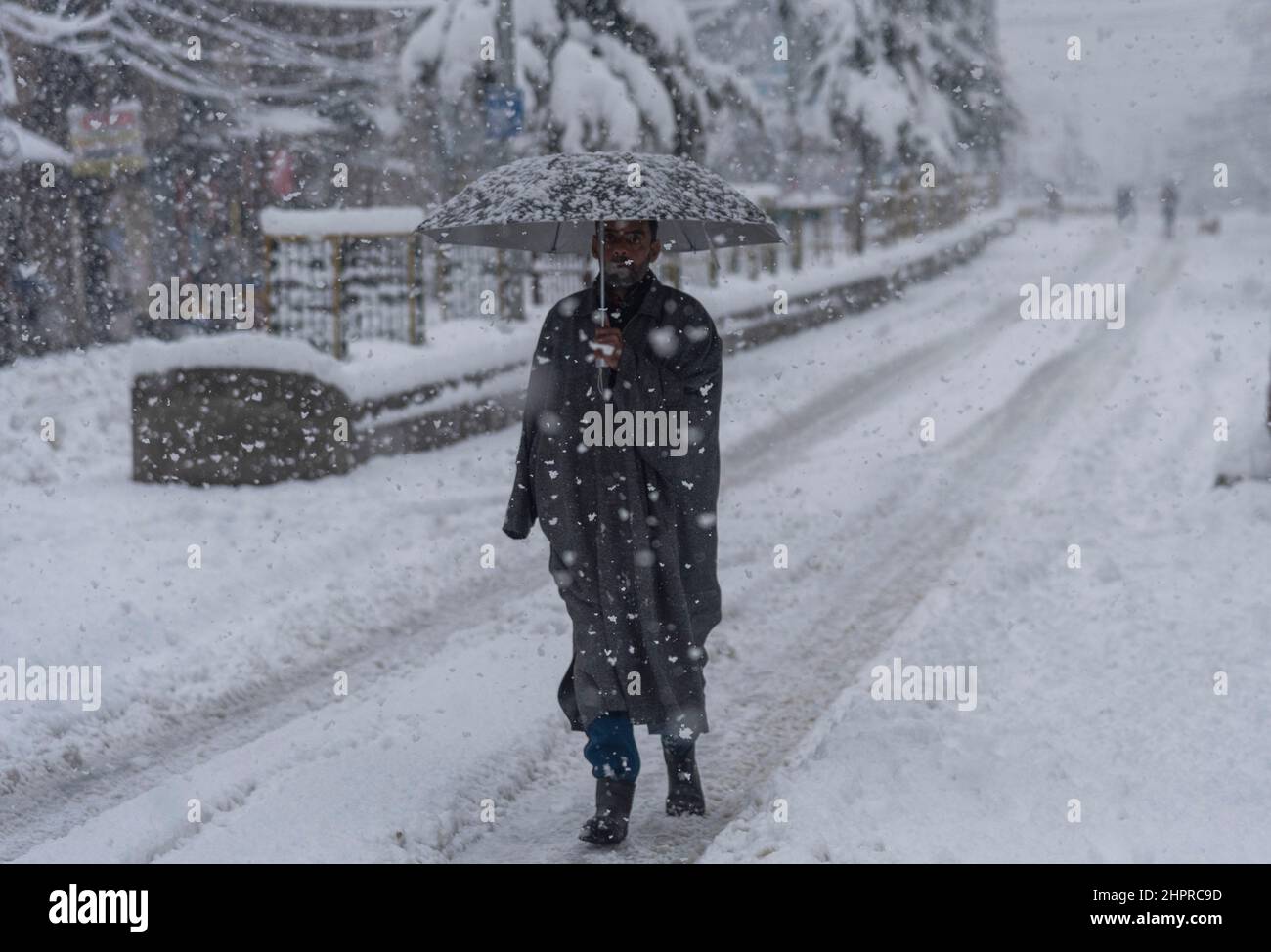 Kashmir, India , 23/02/2022, Srinagar, India. 23rd Feb 2022. Un uomo tiene un ombrello mentre cammina attraverso una strada coperta di neve durante la nevicata pesante in Srinagar.The valle del Kashmir il mercoledì mattina svegliato ad una coperta pesante di nevicata che ha interrotto la vita normale della gente. Le operazioni di volo, il trasporto di superficie e le attività di routine della vita si sono arrestate. Credit: SOPA Images Limited/Alamy Live News Foto Stock
