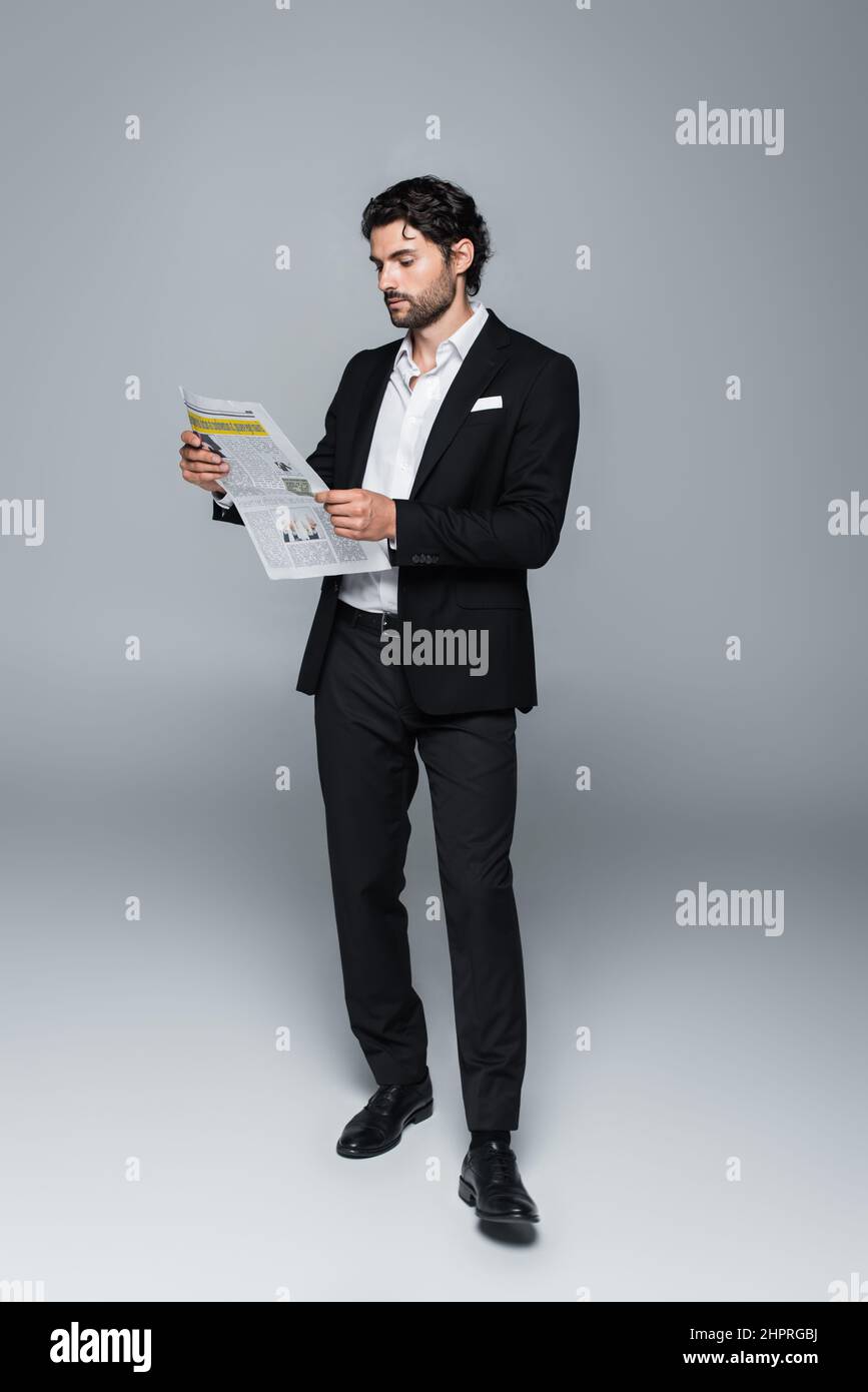 vista a tutta lunghezza dell'uomo in abito nero lettura giornale in grigio Foto Stock