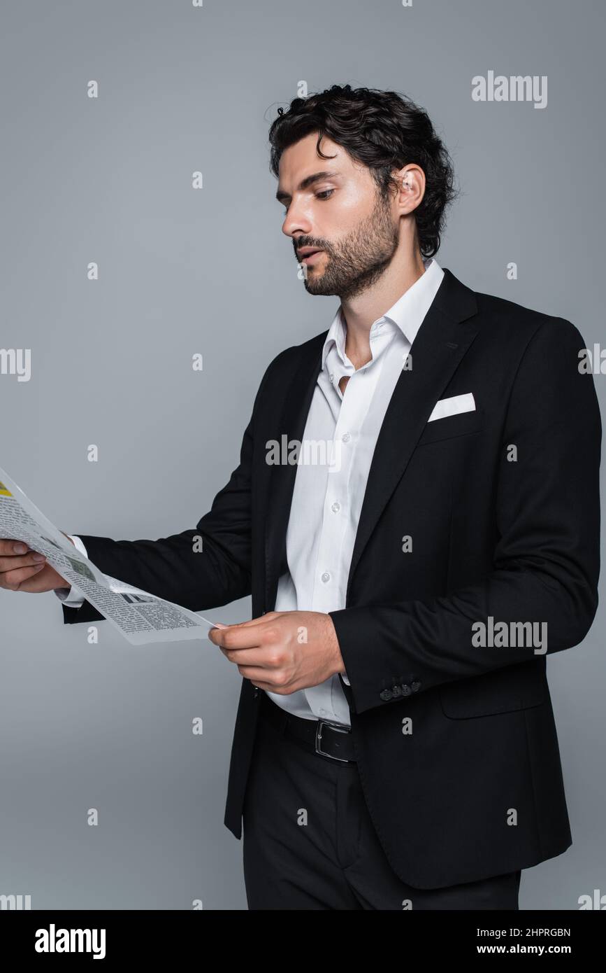 uomo d'affari in blazer nero e camicia bianca lettura giornale isolato su grigio Foto Stock