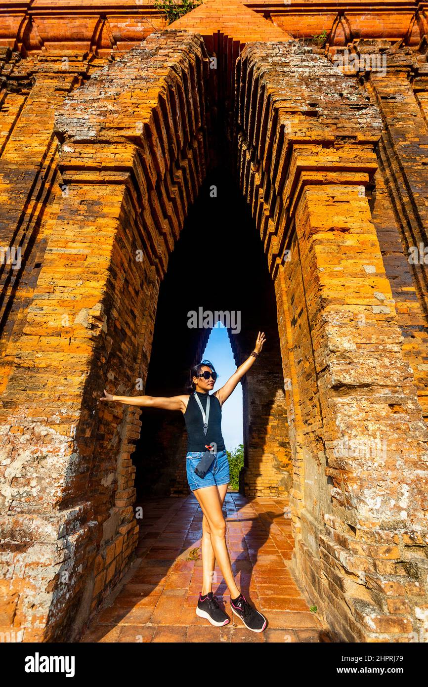 I turisti modellano nell'arco di una Cham Tower indossando pantaloncini jean e la parte superiore nera contro i mattoni dai toni caldi arancioni. Foto Stock